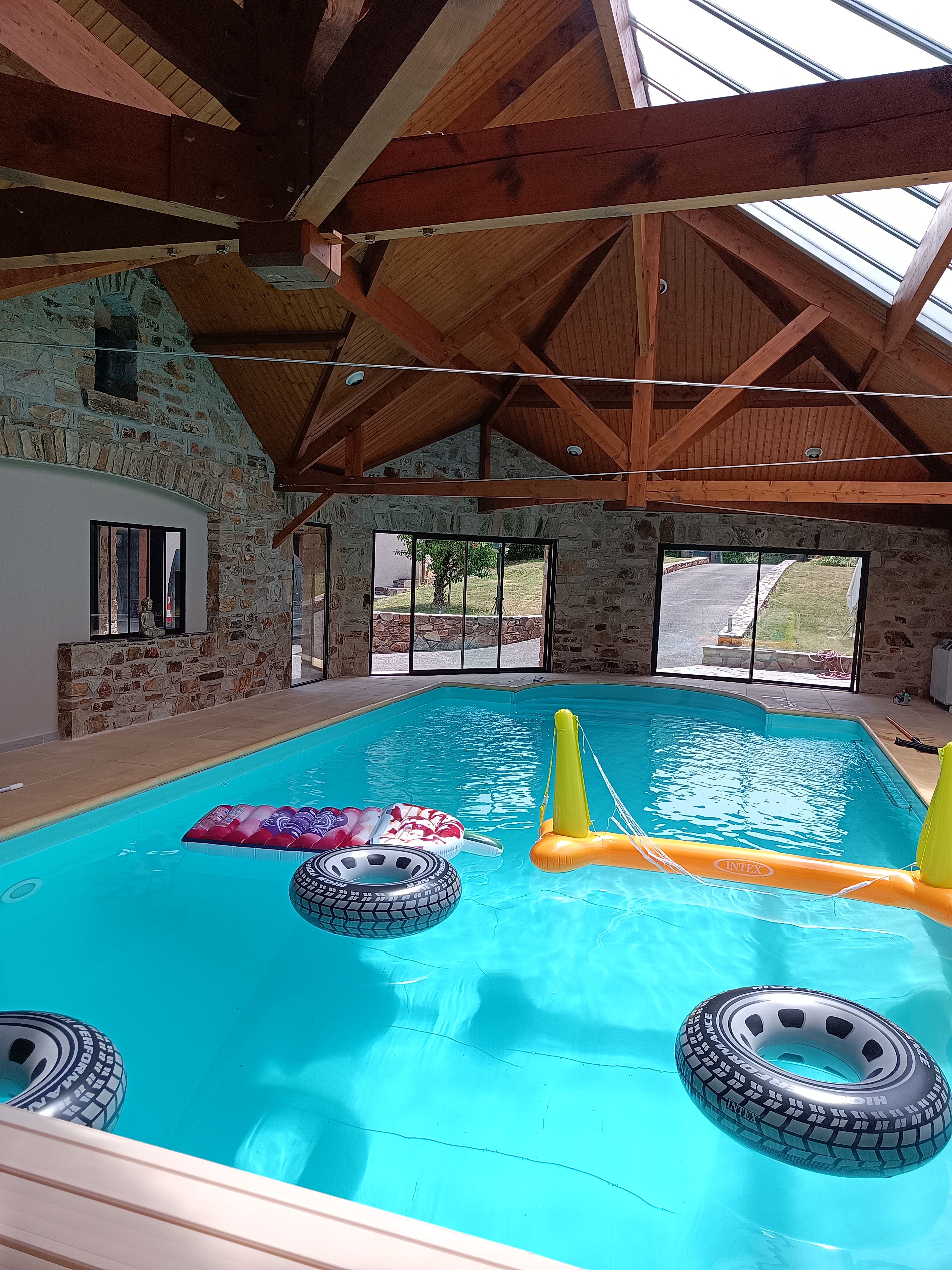 Photo de la piscine couverte, murs en pierre et charpente en bois